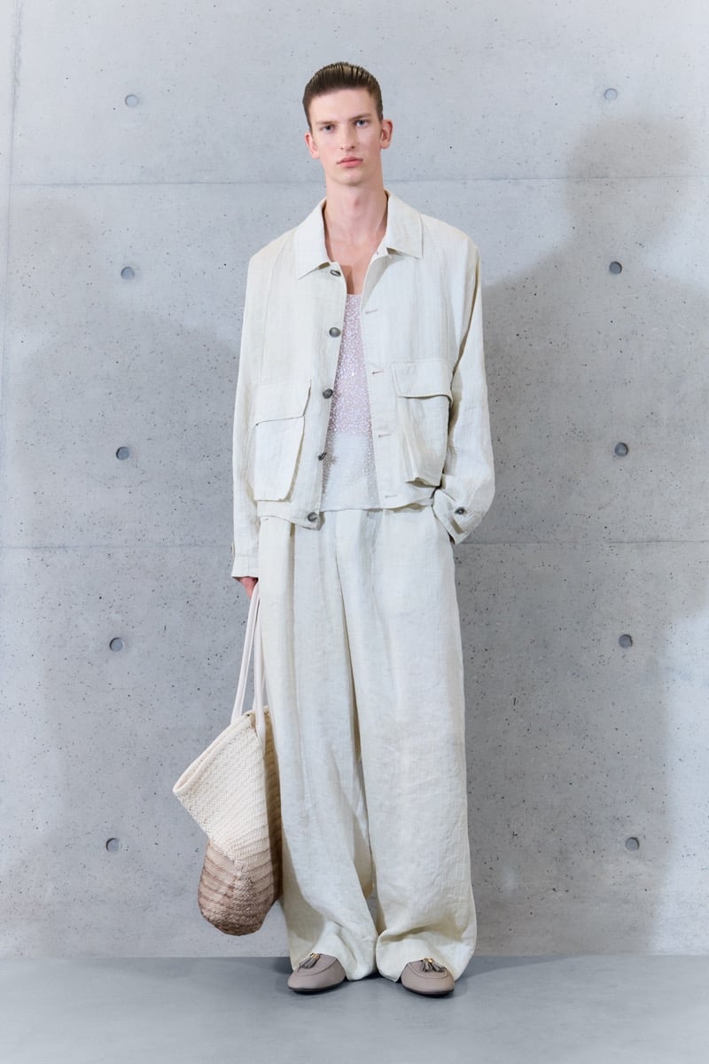 A model in a linen utility jacket over a sequined tank, with wide-leg trousers and a woven tote, for Emporio Armani's spring-summer 2027 collection