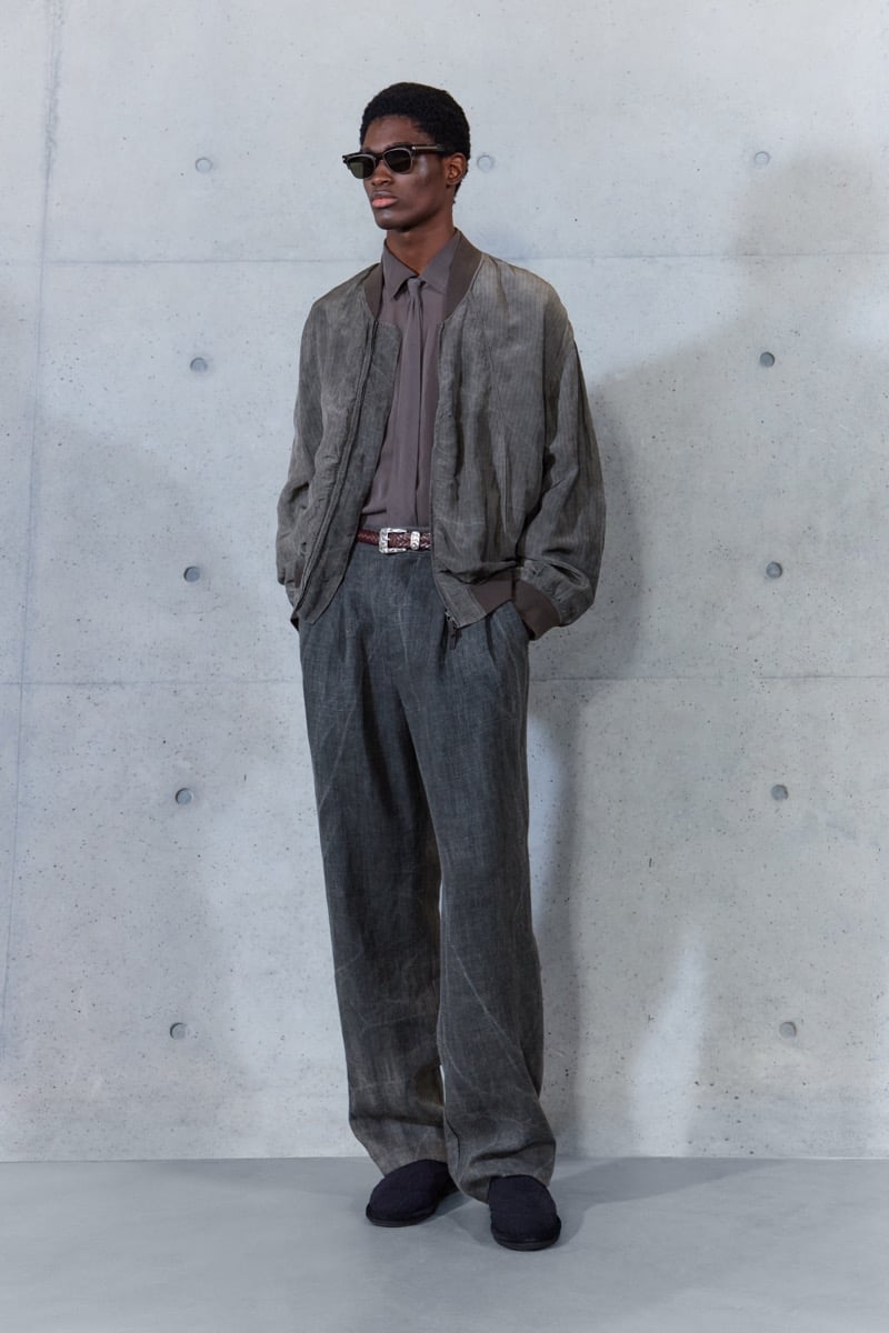 A model in sunglasses and a washed bomber jacket over a shirt, with belted pleated trousers, for Emporio Armani's spring-summer 2027 collection