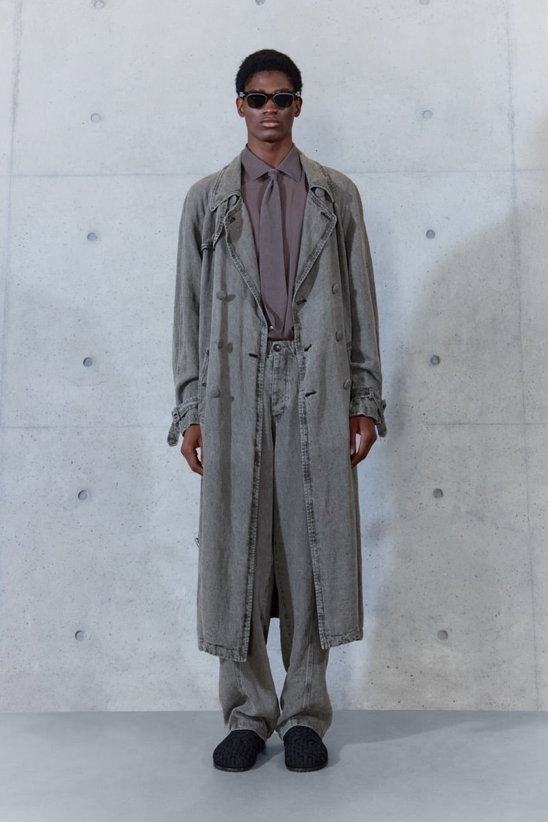 A model in sunglasses and a washed trench coat over a shirt and tie, with matching trousers, for Emporio Armani's spring-summer 2027 collection