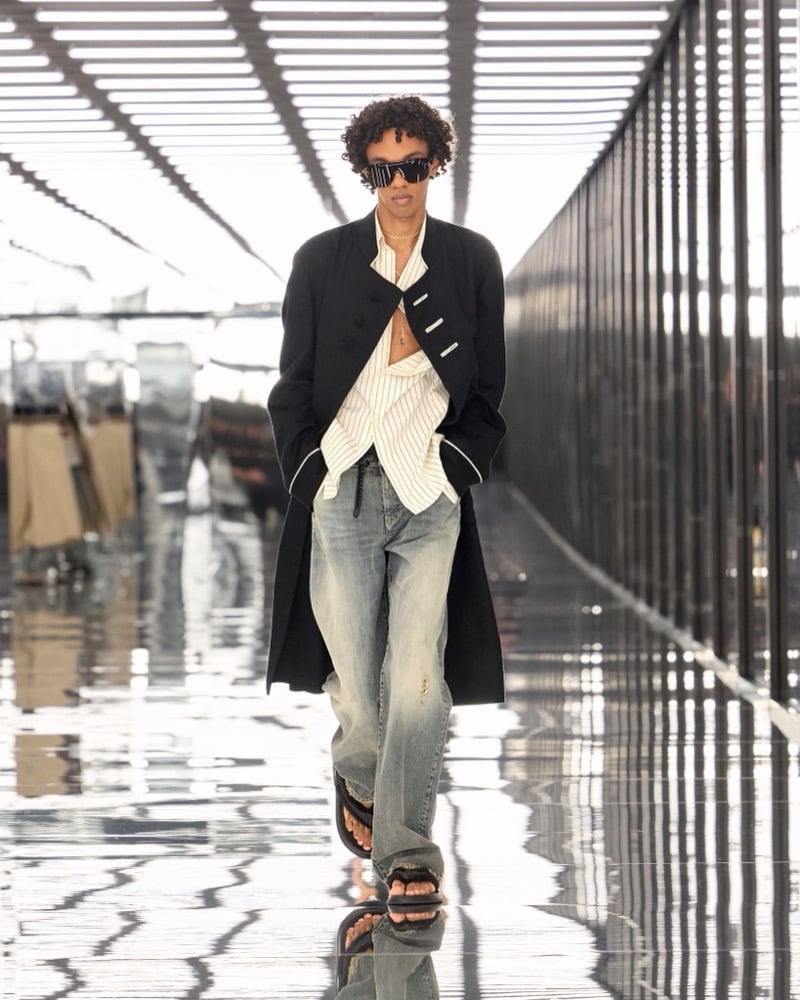 A model in sunglasses and a long military-style coat over a pinstripe shirt, with washed jeans, for Fendi's spring-summer 2027 collection