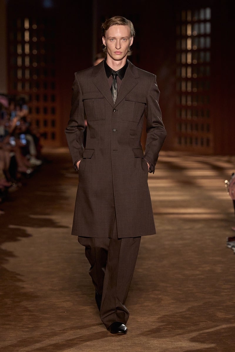 A model in a knee-length coat with bellows pockets over a shirt and tie, with wide trousers, for Ferragamo's spring-summer 2027 collection