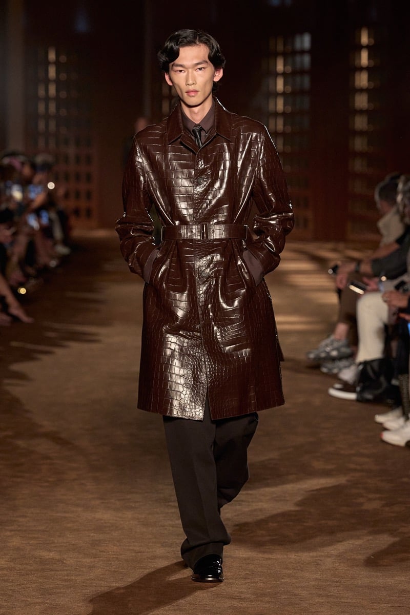 A model in a belted brown crocodile coat over a shirt and tie, with wide trousers, for Ferragamo's spring-summer 2027 collection