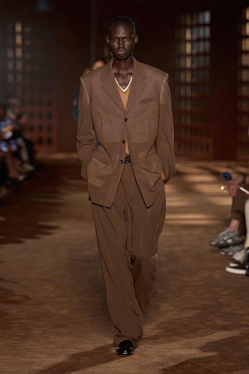 A model in a sheer brown suit over a V-neck knit, with wide pleated trousers, for Ferragamo's spring-summer 2027 collection