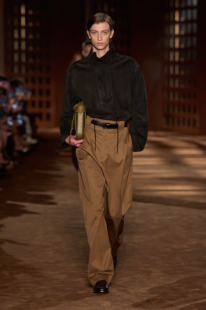 A model in a suede drawstring pullover and belted pleated trousers, holding an olive leather bag, for Ferragamo's spring-summer 2027 collection