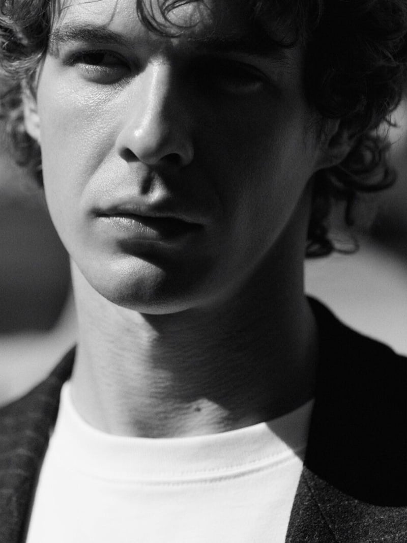 Tight black-and-white portrait of Efraim Schröder's face, curly hair and a white crew-neck top with a dark jacket collar just visible at the shoulder