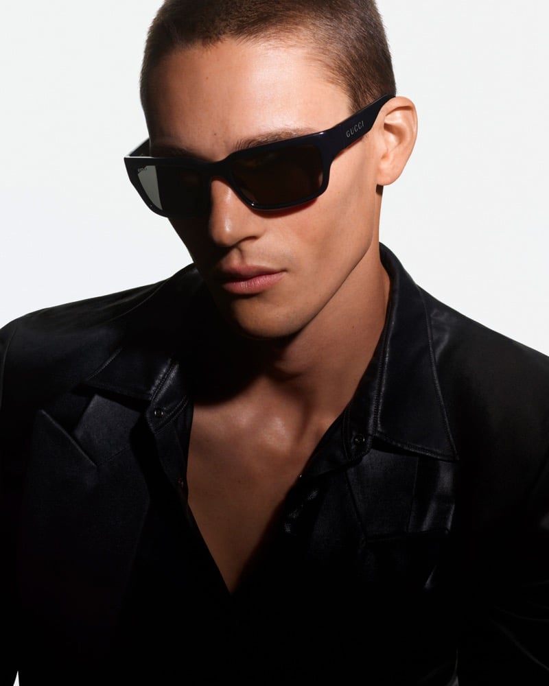 Samuel Watson wears black rectangular Gucci sunglasses and a black leather shirt jacket in a shadow-lit portrait for Gucci Fall-Winter 2026 eyewear.