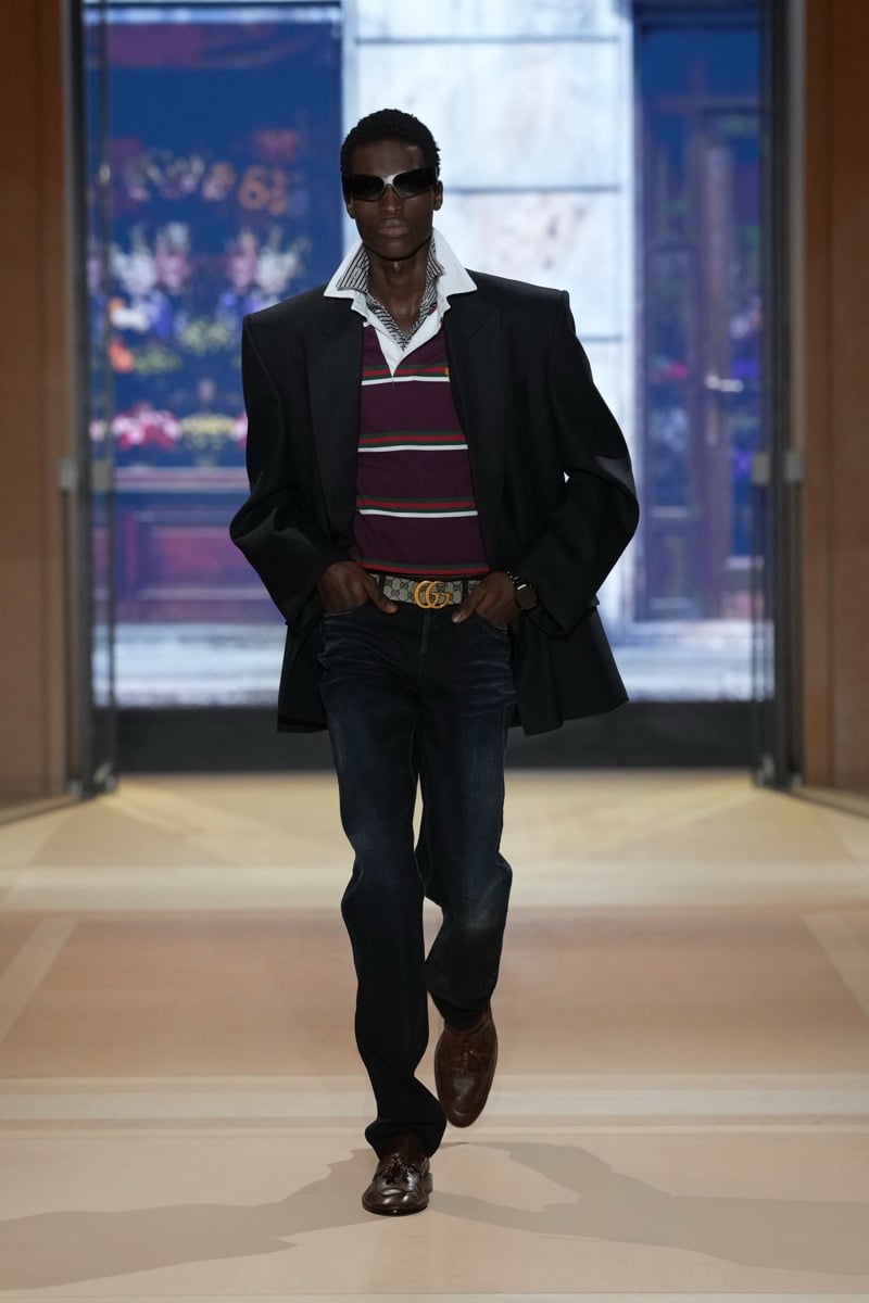 A model in a blazer over a striped rugby shirt, with a GG belt, jeans, and tassel loafers, for Gucci's spring-summer 2027 collection