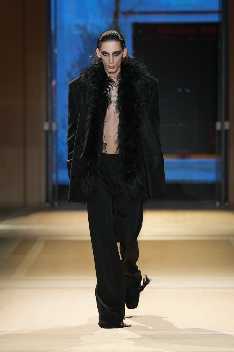 A model in a feather-trimmed jacket over a bare chest, with wide trousers and fringed slippers, for Gucci's spring-summer 2027 collection