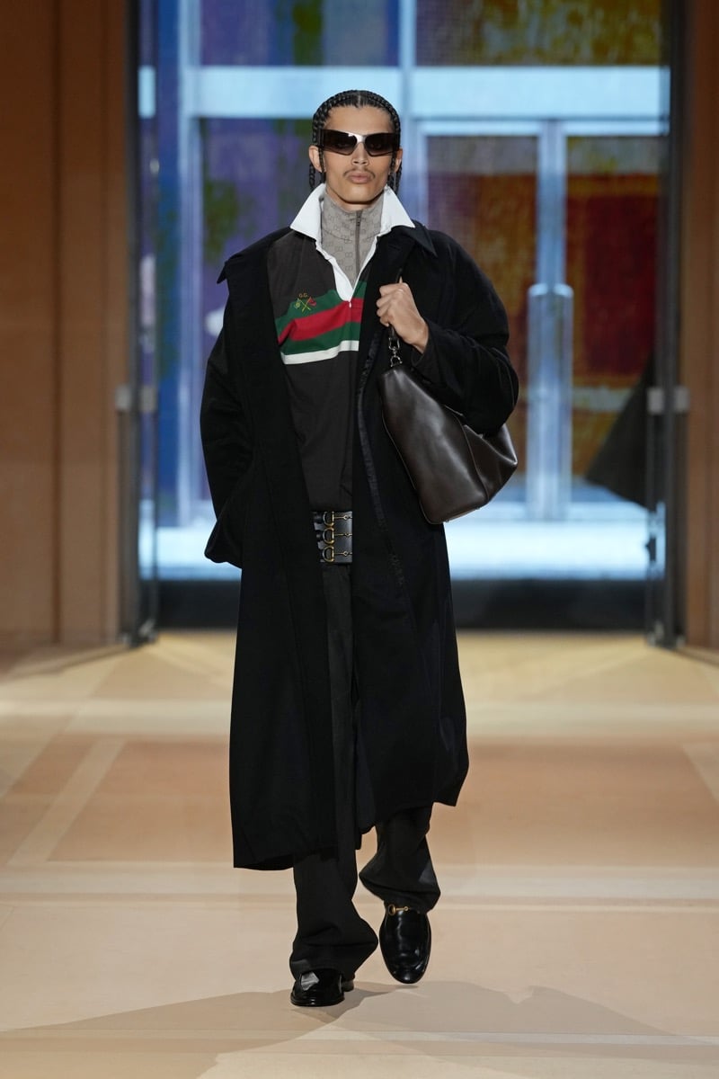 A model in a long coat over a Web-stripe rugby shirt, with a triple Horsebit belt and leather shoulder bag, for Gucci's spring-summer 2027 collection