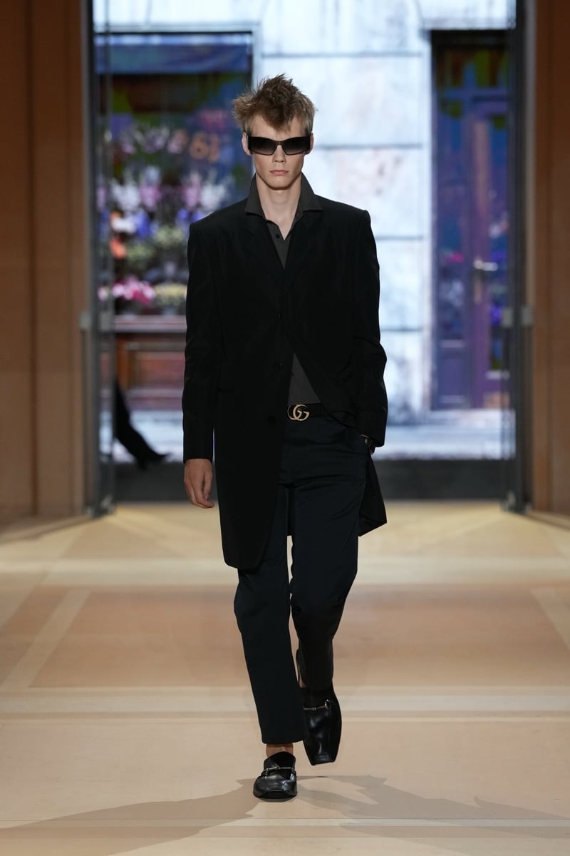 A model in a long jacket over a shirt, with a GG belt, cropped trousers, and Horsebit loafers, for Gucci's spring-summer 2027 collection