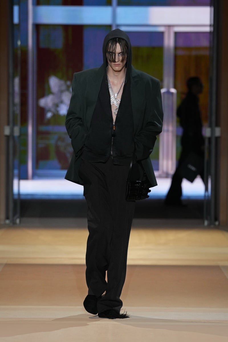 A model in an oversized blazer over a zip hoodie and Gucci script chain, with wide trousers, for Gucci's spring-summer 2027 collection