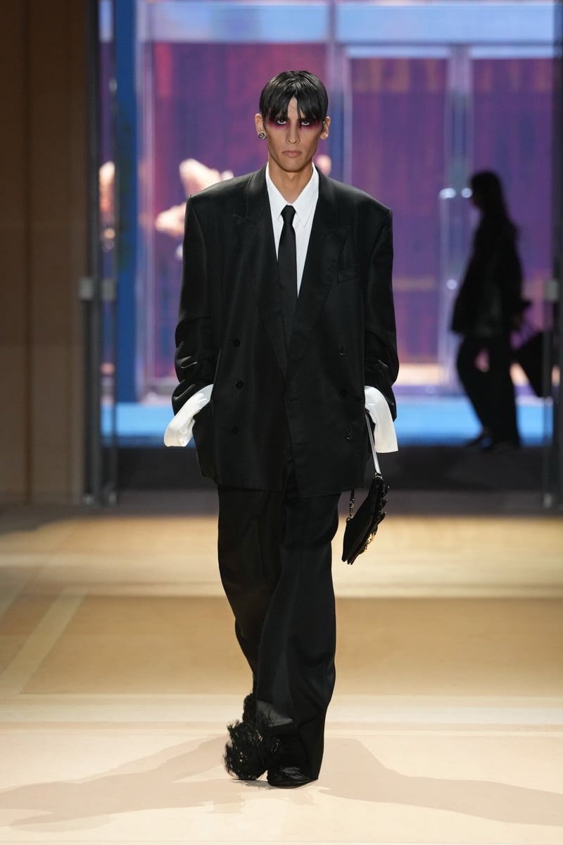 A model in an oversized double-breasted suit with a tie and extended shirt cuffs, holding a small bag, for Gucci's spring-summer 2027 collection