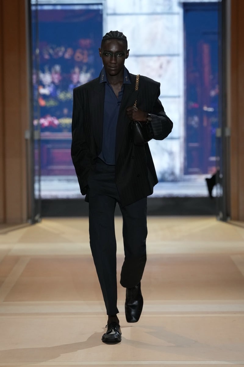 A model in a pinstripe blazer over an open shirt, with a chain-strap shoulder bag and cropped trousers, for Gucci's spring-summer 2027 collection