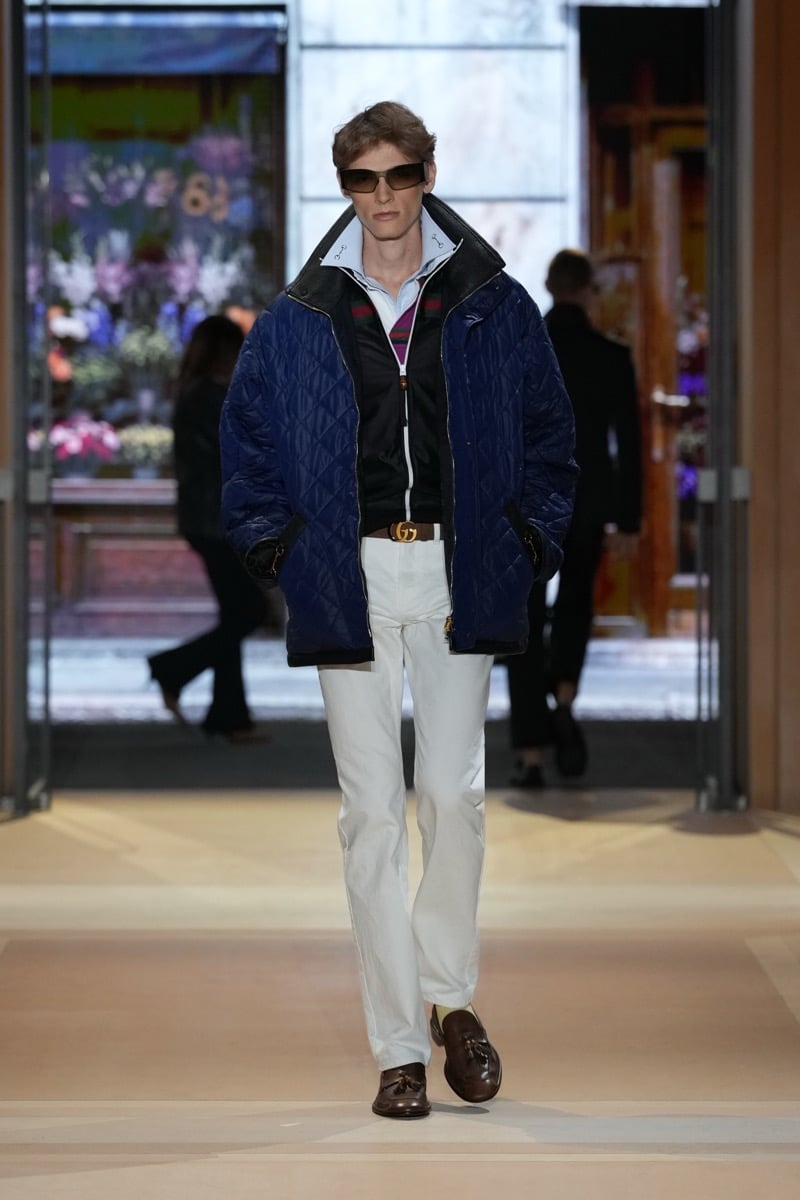 A model in a quilted jacket over a zip track jacket, with a GG belt, jeans, and tassel loafers, for Gucci's spring-summer 2027 collection