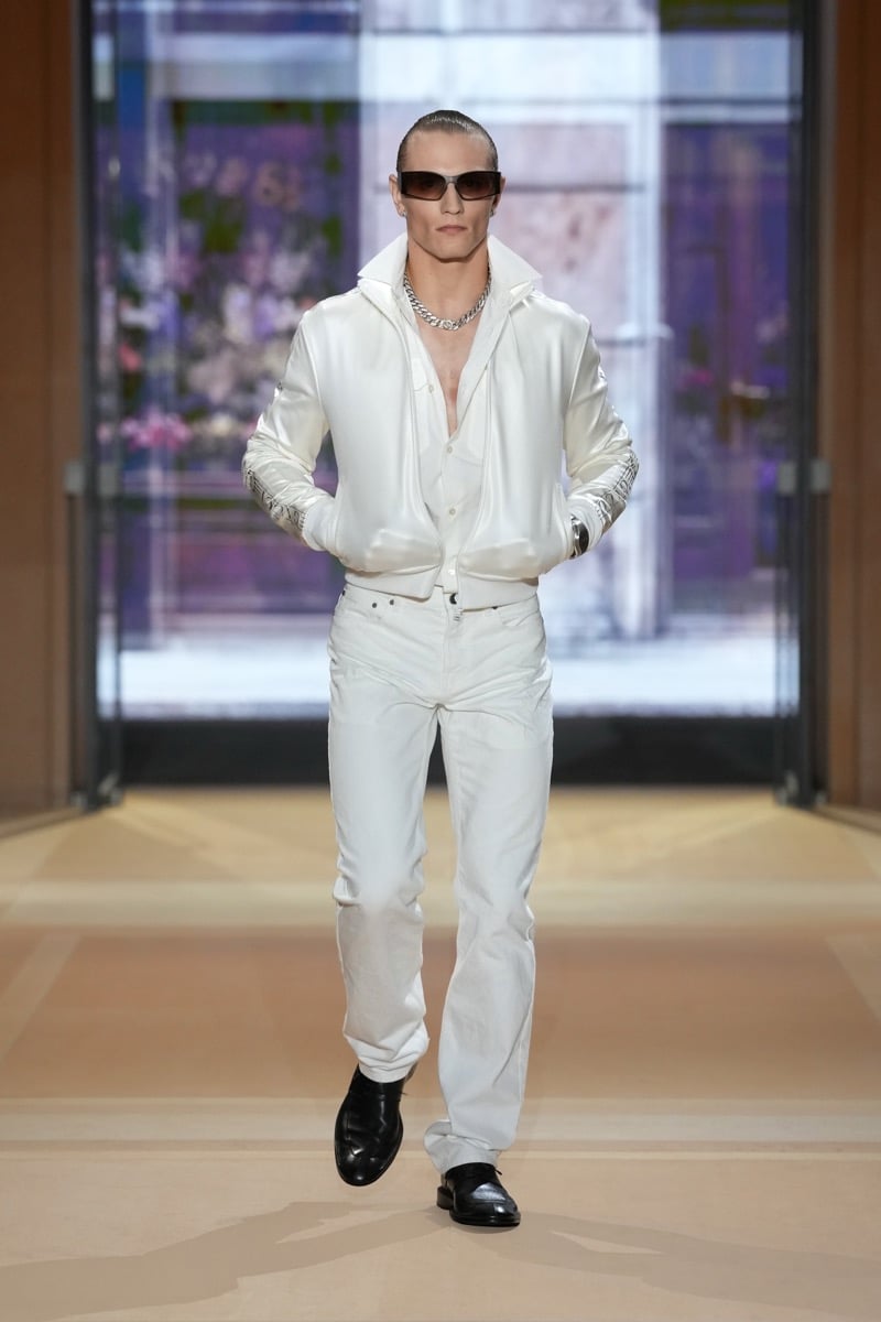 A model in a satin bomber jacket over an open shirt and chain necklace, with jeans, for Gucci's spring-summer 2027 collection