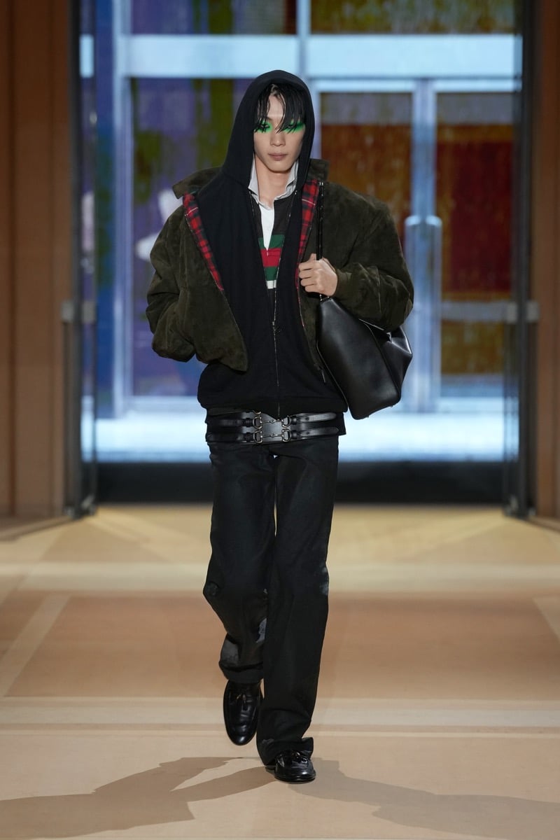 A model in a suede bomber with tartan trim over a hoodie, with a triple Horsebit belt and leather bag, for Gucci's spring-summer 2027 collection