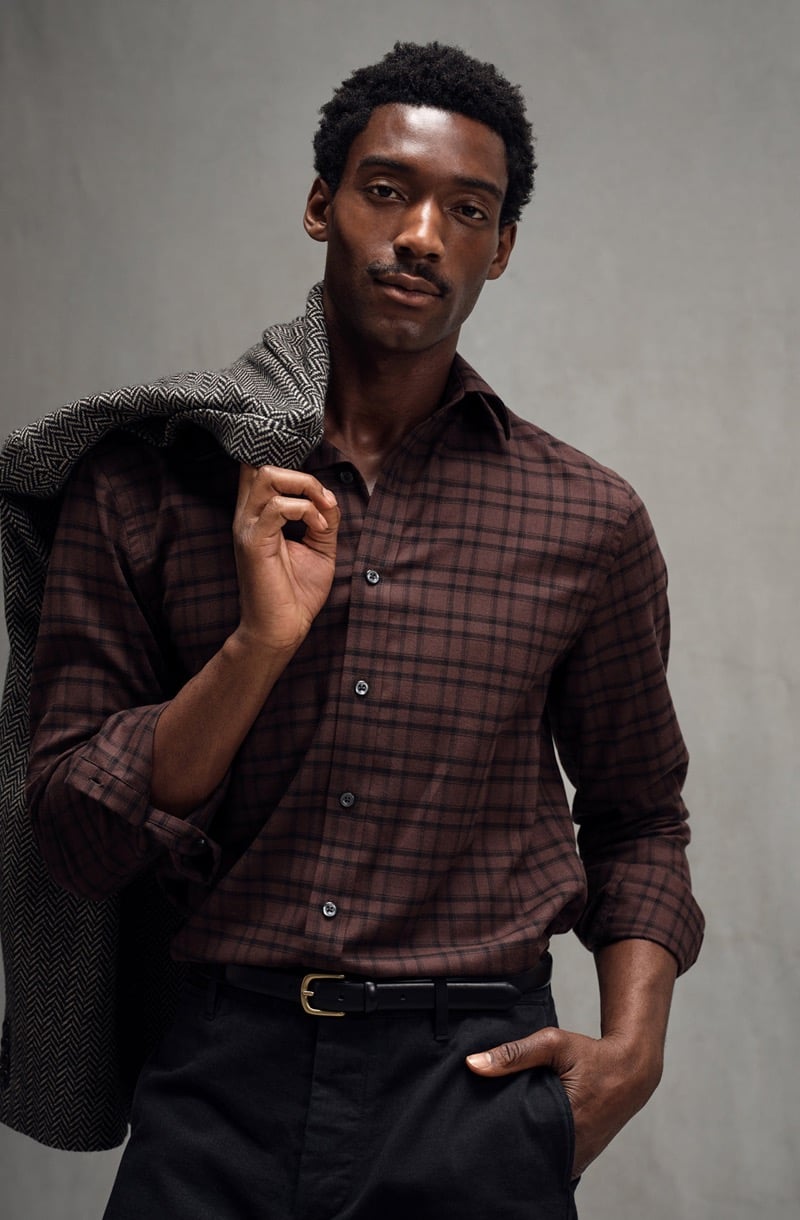 Halid Nuhu wears a plaid sport shirt with a herringbone jacket slung over his shoulder and a hand in his pocket, for Todd Snyder's Essential Pieces