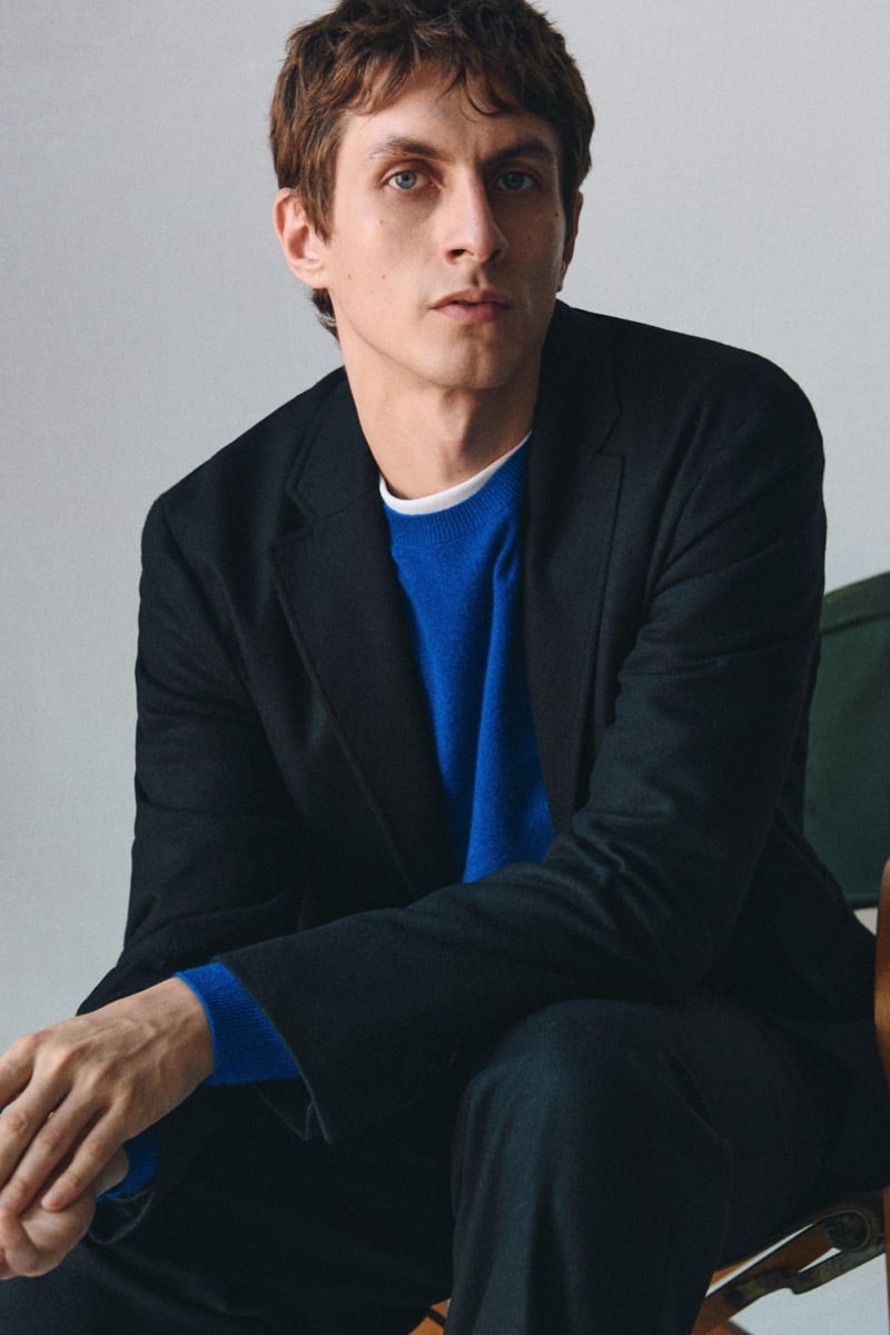 Henry Kitcher sits in a dark blazer over a bright blue crewneck sweater, for Massimo Dutti's The Loft
