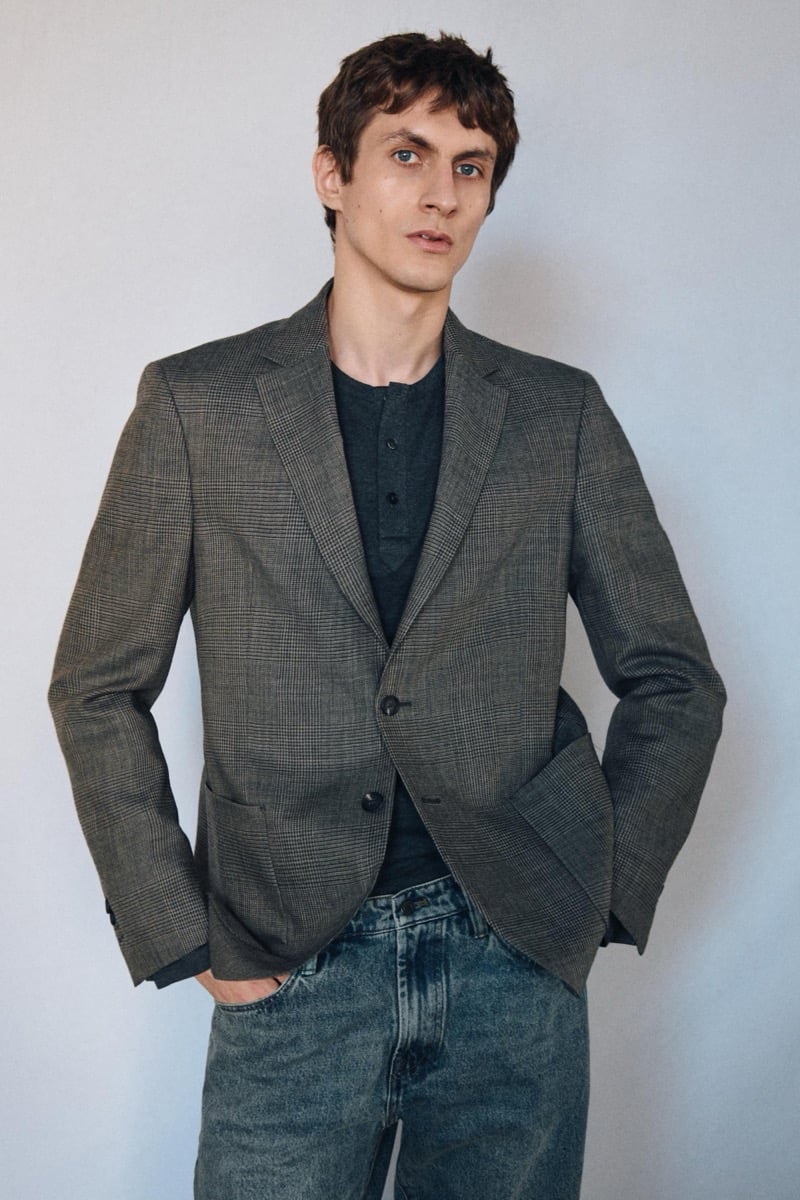 Henry Kitcher stands with his hands in his pockets in a glen plaid blazer over a henley with faded jeans, for Massimo Dutti's The Loft