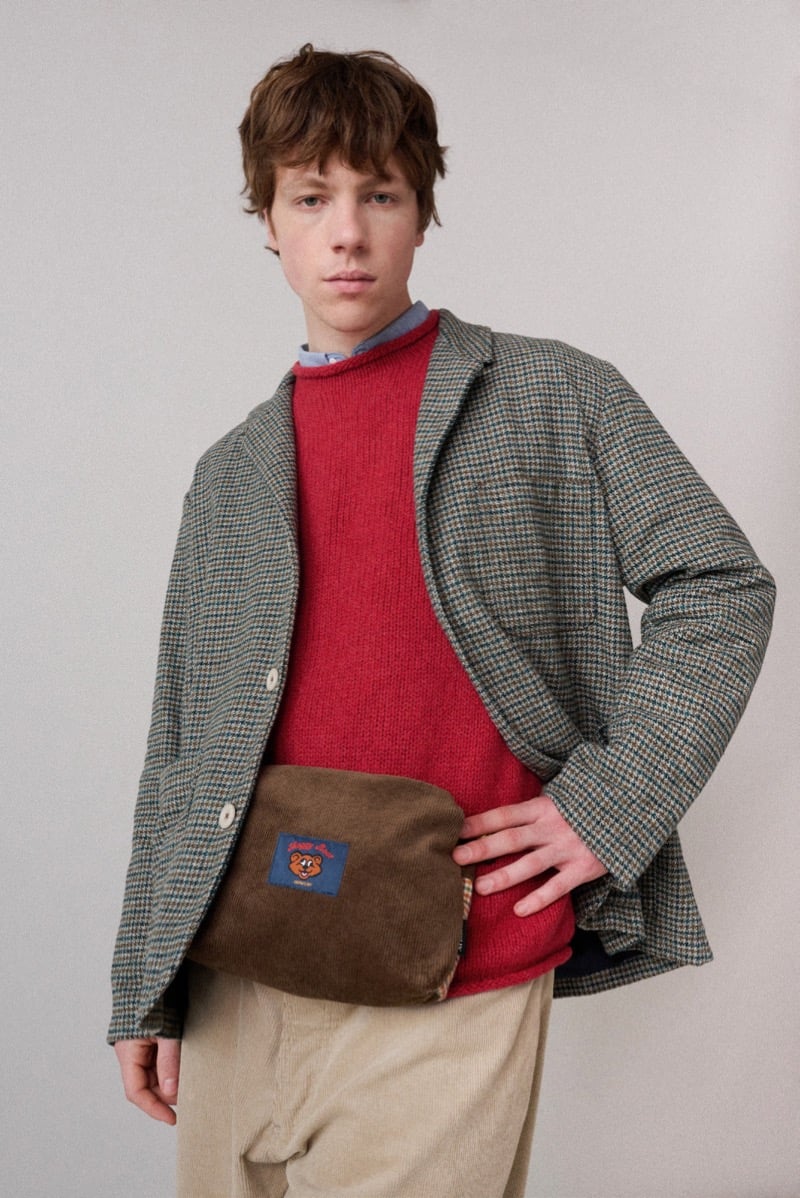 A model in a checked blazer over a red sweater, with a corduroy crossbody bag and trousers, for Howlin's fall-winter 2026 collection