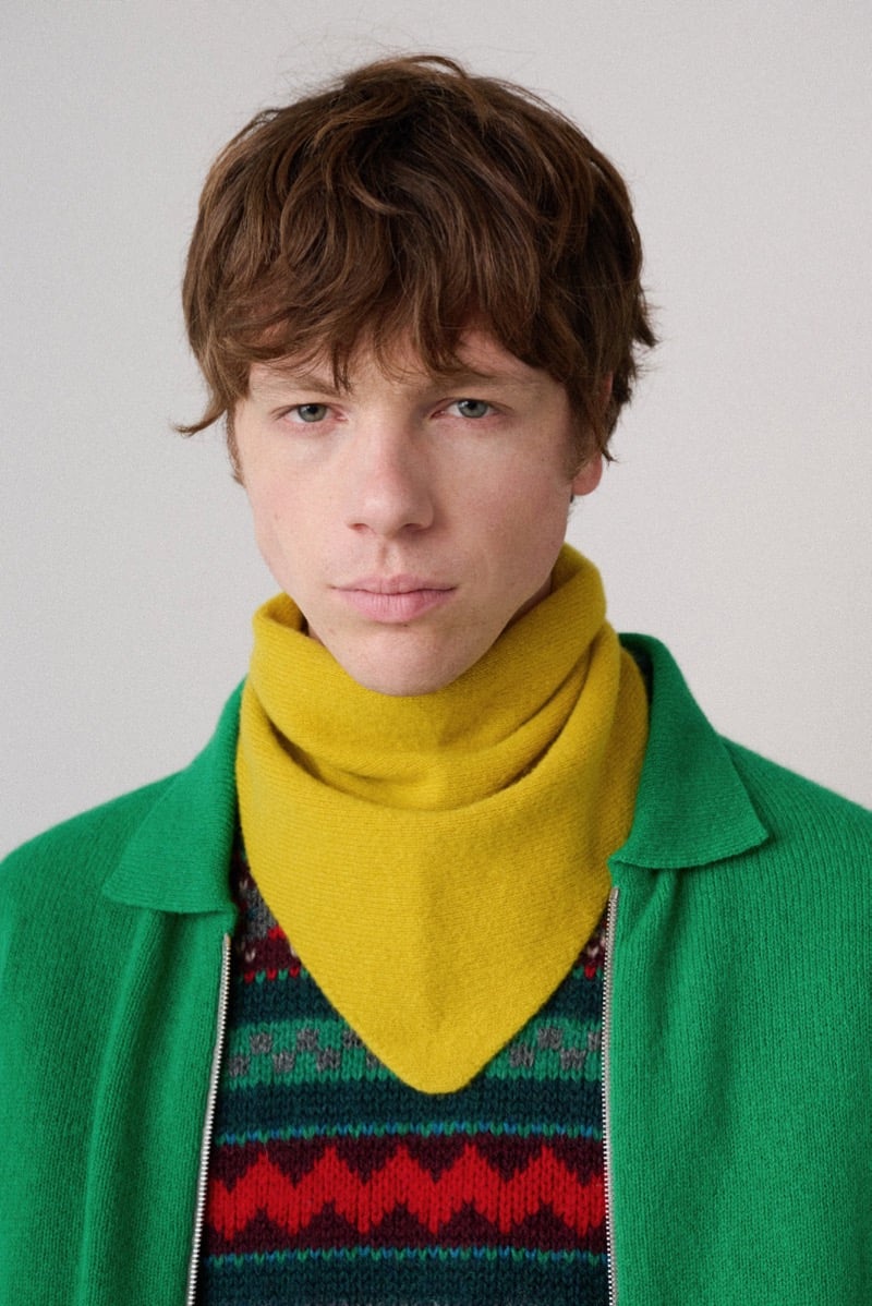 A model in a green overshirt worn open over a patterned sweater, with a mustard knit scarf, for Howlin's fall-winter 2026 collection