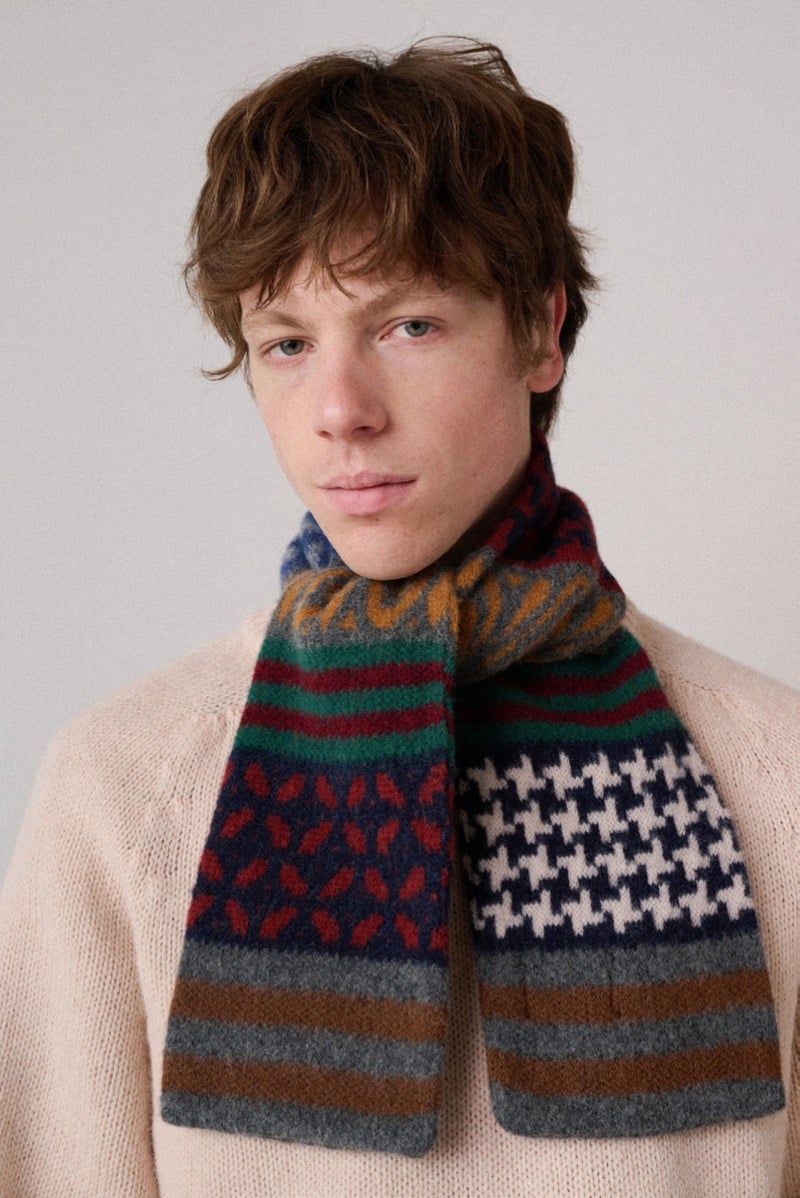 A model in a light-colored sweater with a multicolor patterned scarf wrapped around the neck, for Howlin's fall-winter 2026 collection