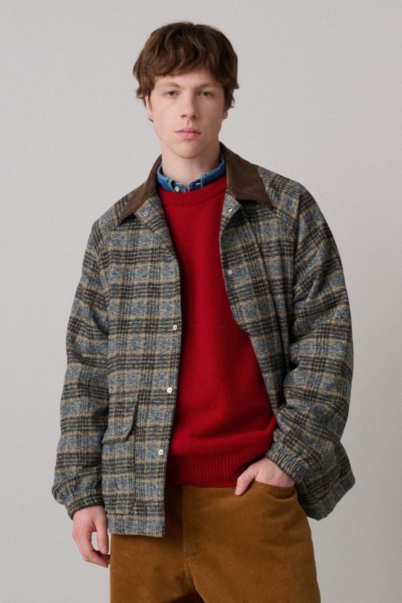 A model in a plaid wool jacket with a corduroy collar, layered over a red sweater, for Howlin's fall-winter 2026 collection
