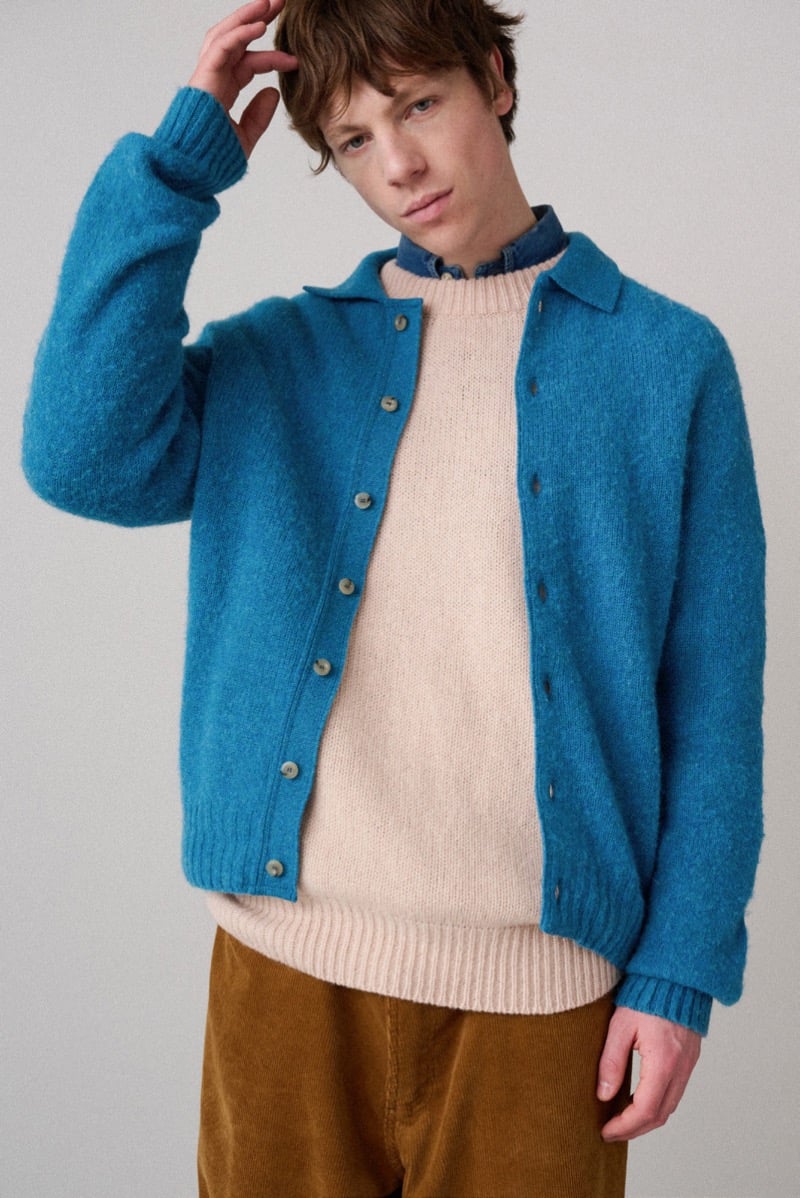 A model in a teal cardigan layered over a lighter knit sweater and a denim collar, for Howlin's fall-winter 2026 collection