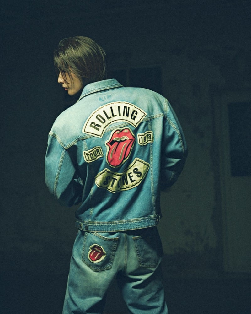 Hyunjin seen from behind in a light-wash denim jacket with a large Rolling Stones tongue tour patch across the back, worn with matching patched jeans, for GUESS JEANS x The Rolling Stones