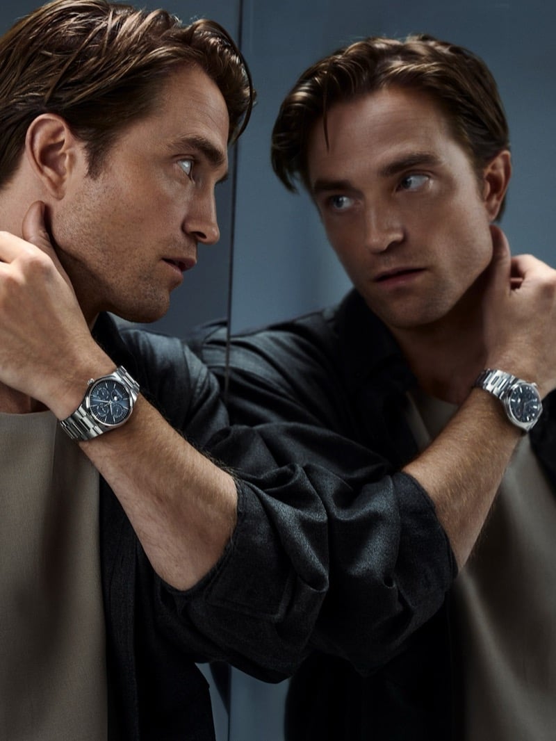 Robert Pattinson looking at his reflection in a mirror, hand at his neck, with a steel Jaeger-LeCoultre watch on his wrist