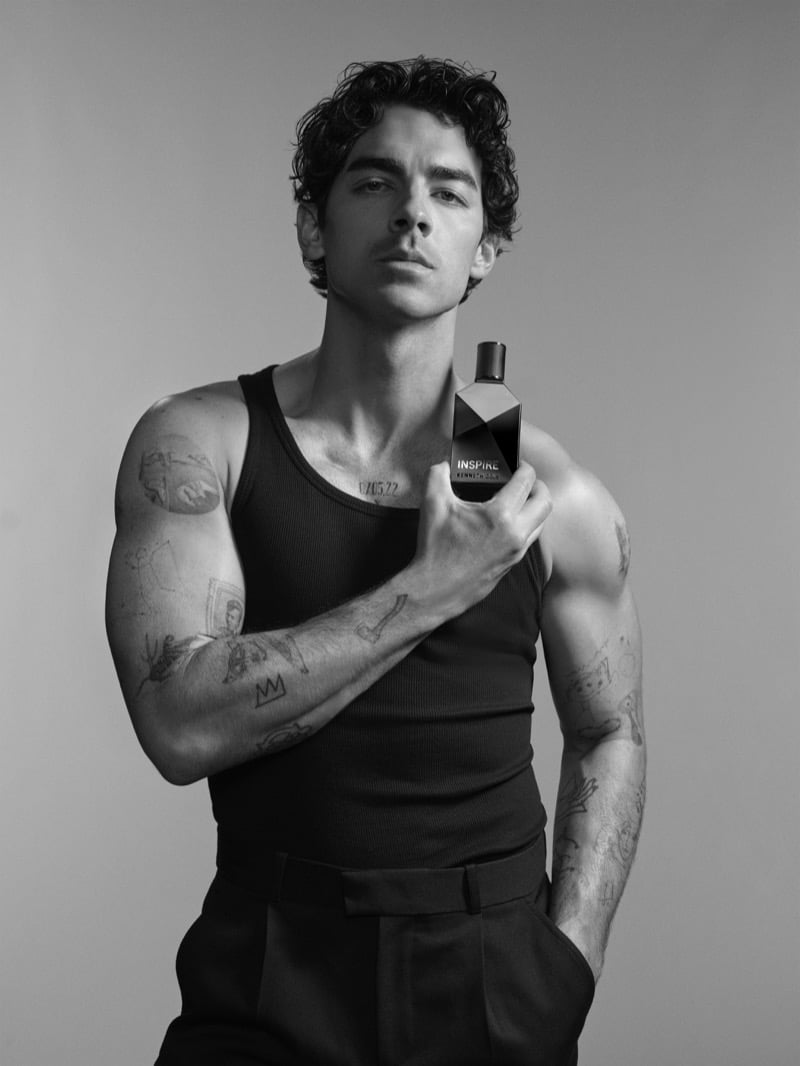Joe Jonas holds a bottle of Kenneth Cole INSPIRE to his chest in a ribbed tank top and pleated trousers.