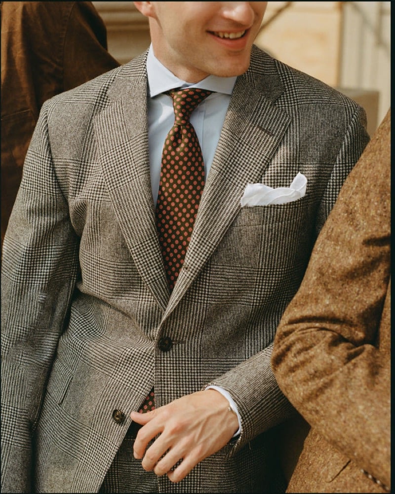 A detail of two models in tweed, the nearer in a gray glen-check sport coat with a light blue shirt, a brown foulard tie, and a pocket square, for J. Press fall-winter 2026
