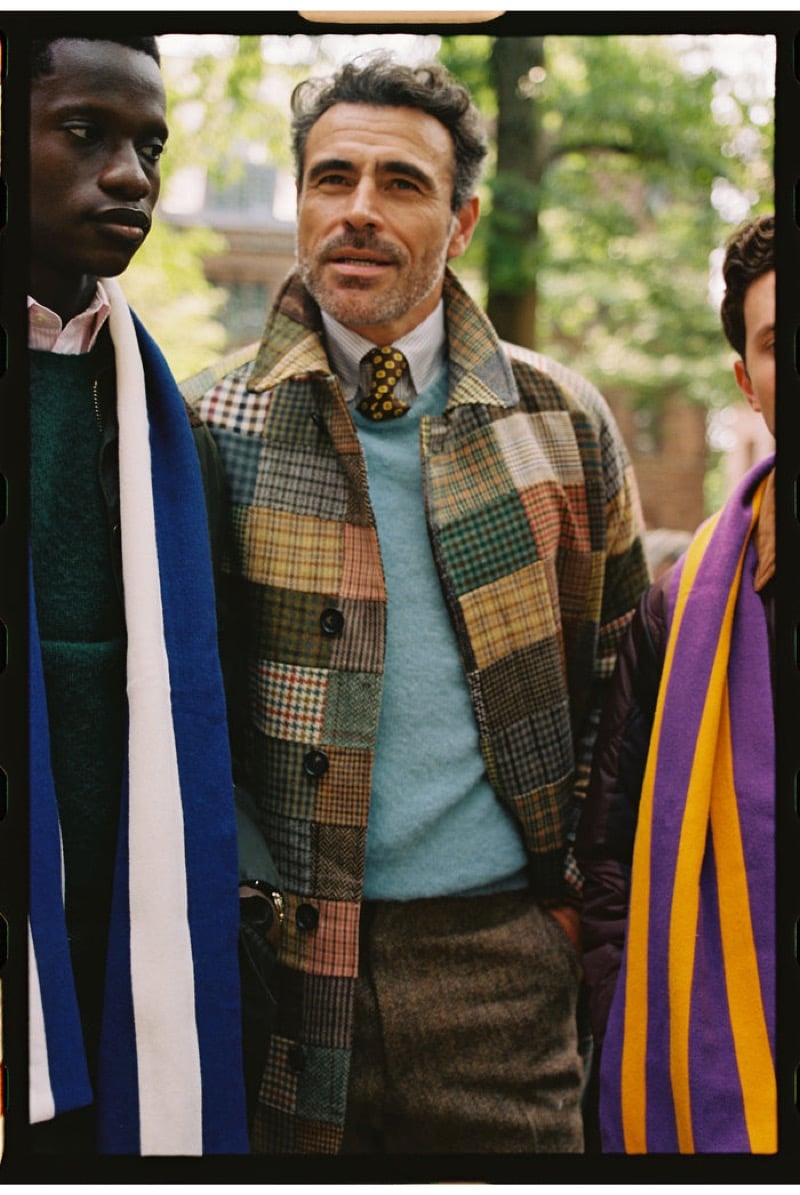 Three models outdoors, the center one in a patchwork tweed jacket of mixed checks over a light blue sweater and a striped shirt with a yellow dot tie, flanked by college-striped scarves, for J. Press fall-winter 2026