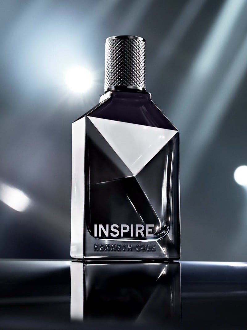 The faceted Kenneth Cole INSPIRE men's fragrance bottle with a knurled cap, lit by spotlights.