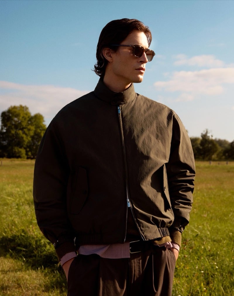 Liam Kelly in sunglasses and a Harrington jacket over a checked shirt in an open field