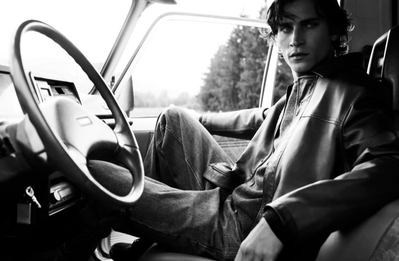 Black-and-white photo of Liam Kelly in a leather jacket and jeans sitting in the driver's seat of an old four-wheel drive