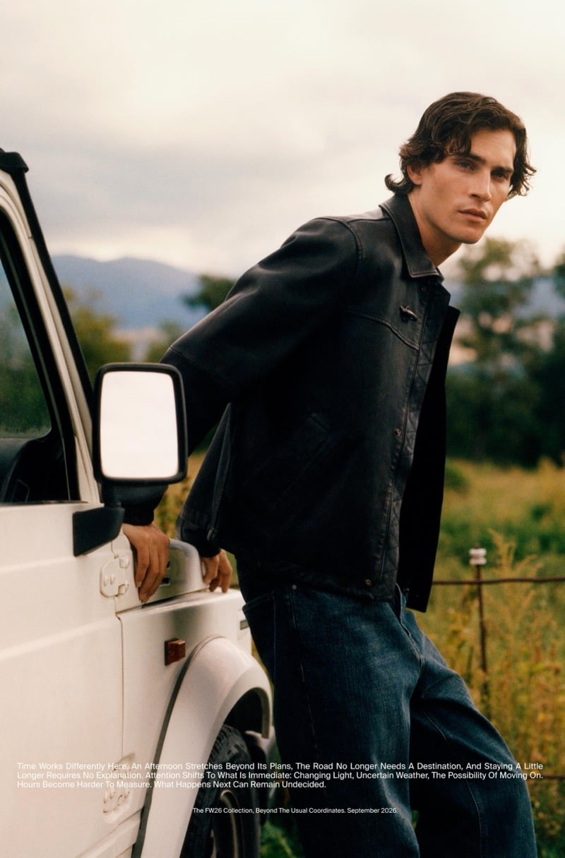 Liam Kelly in a leather jacket and jeans leaning against an old four-wheel drive in the countryside
