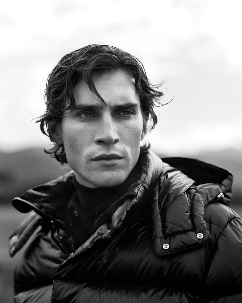 Black-and-white close-up of Liam Kelly in a glossy puffer jacket and turtleneck