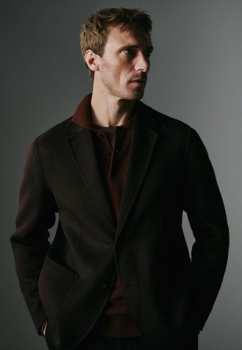 Clément Chabernaud photographed in low light wearing a dark brown wool blazer over a rust-brown knit polo