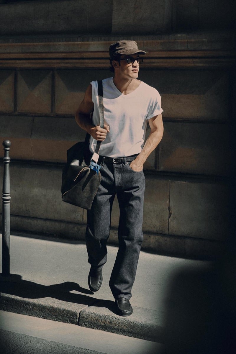 Max Knott in a flat cap and sunglasses, wearing a white tee and jeans with a shoulder bag for Zara's 90's Archive