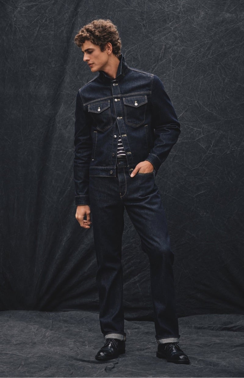 Max Mersmann glances to the side in a dark denim Dylan jacket over a striped tee with matching cuffed jeans and black lace-up shoes, for Todd Snyder's Essential Pieces