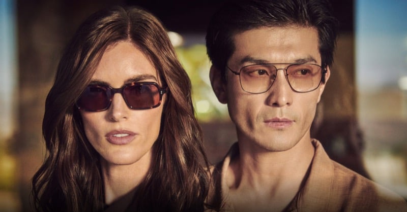 Hilary Rhoda in Oliver Peoples' rectangular tortoise Larell sunglasses stands beside Daisuke Ueda in thin gold-rimmed Aymes sunglasses, backlit by golden dusk light, from the brand's fall 2026 Twice Upon a Time story