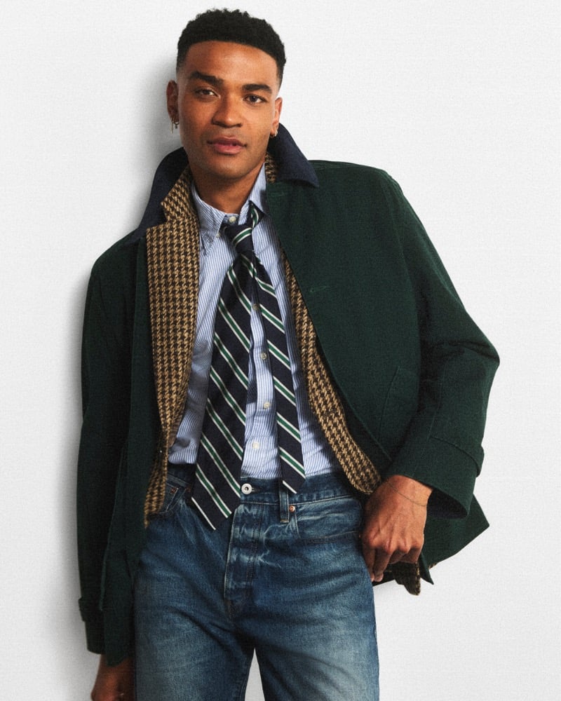 Owen Thiele in a green J.Crew Barn Jacket over a houndstooth blazer, striped shirt, striped tie, and jeans