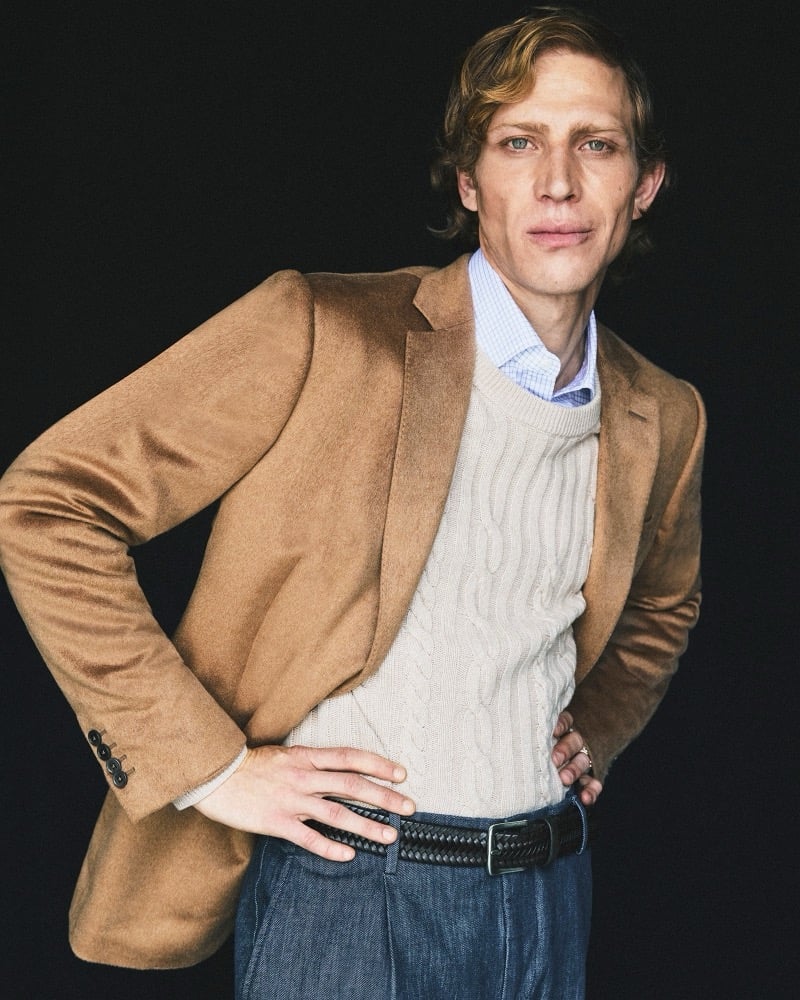 Mike Vasilakis wears a camel blazer over a cable-knit sweater, hands on his hips, for Pal Zileri's fall-winter 2026 campaign.