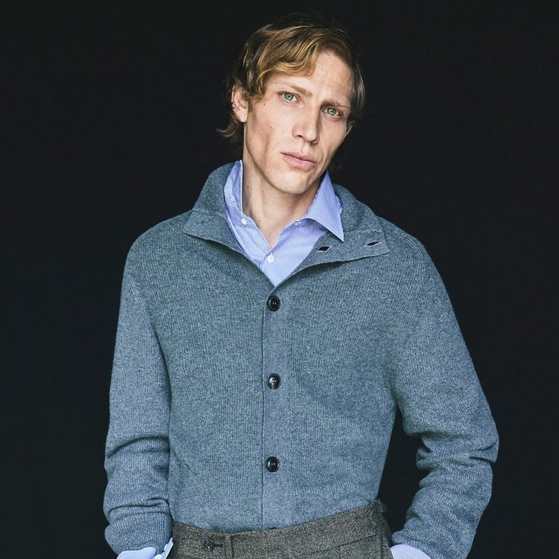 Mike Vasilakis wears a charcoal funnel-neck cardigan over a checked shirt for Pal Zileri's fall-winter 2026 campaign.