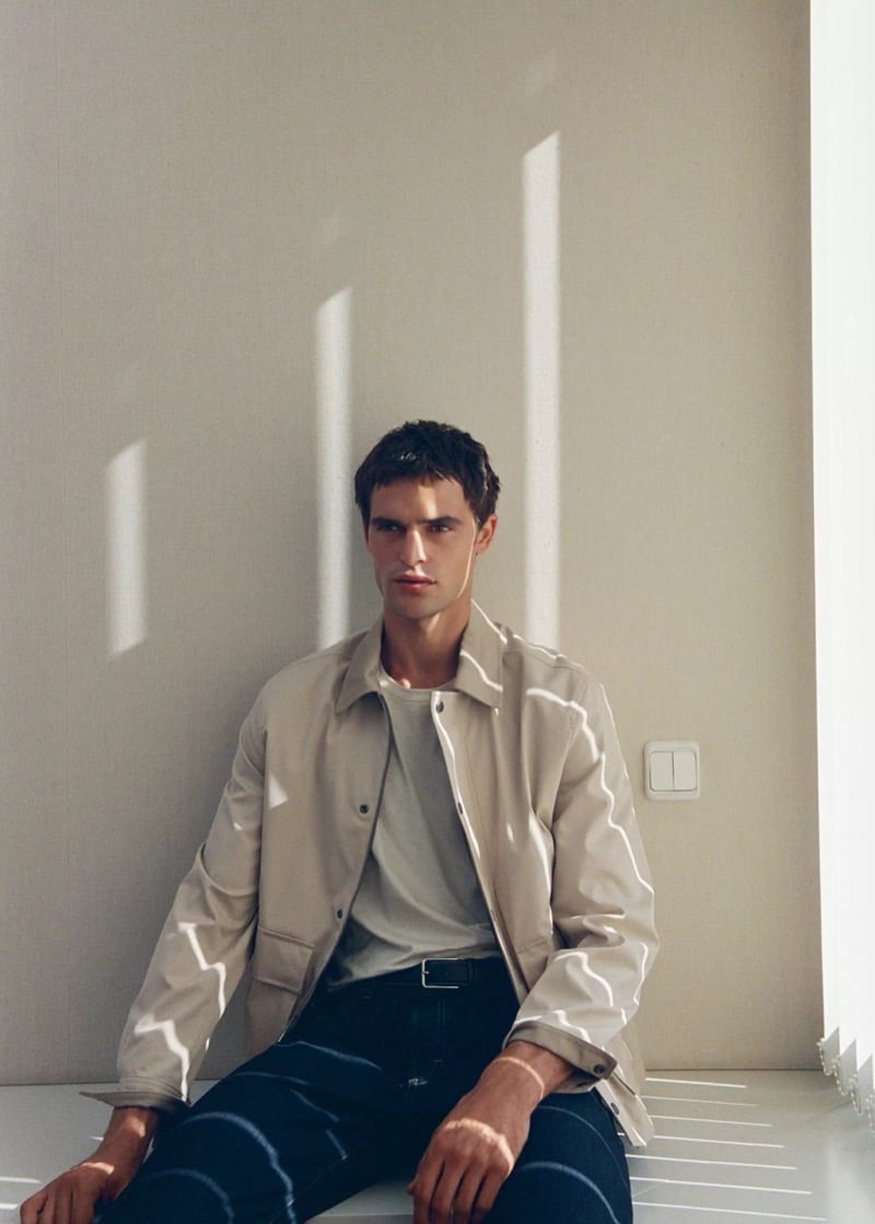 Parker van Noord seated in a beige water-repellent jacket over a tee and dark jeans with stripes of sunlight across the wall