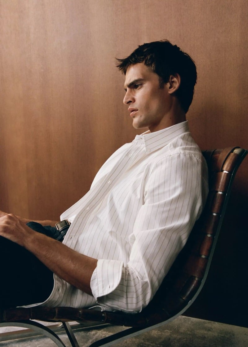 Parker van Noord in profile leaning back in a leather chair in an open-collar pinstripe shirt