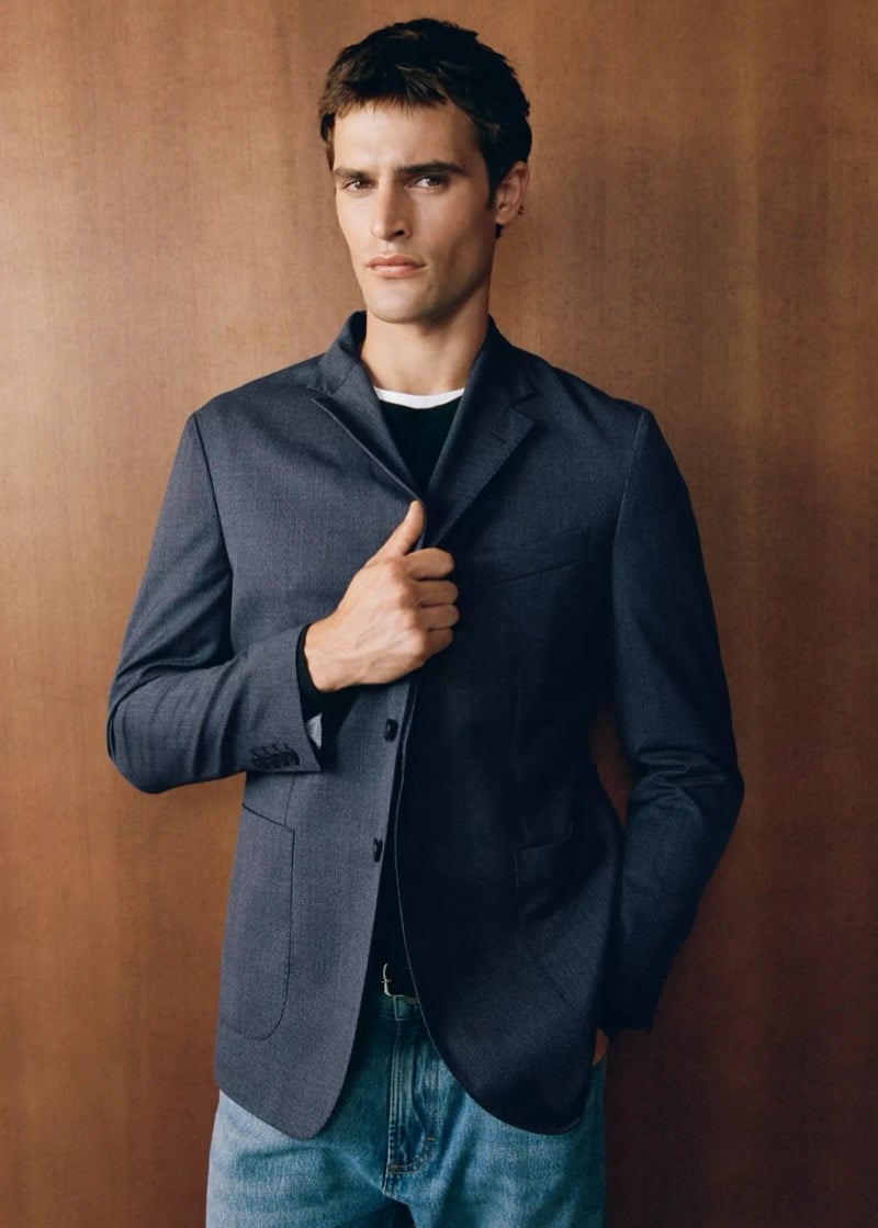Parker van Noord holding the lapel of a gray-blue wool-blend blazer over a dark tee with light-wash jeans