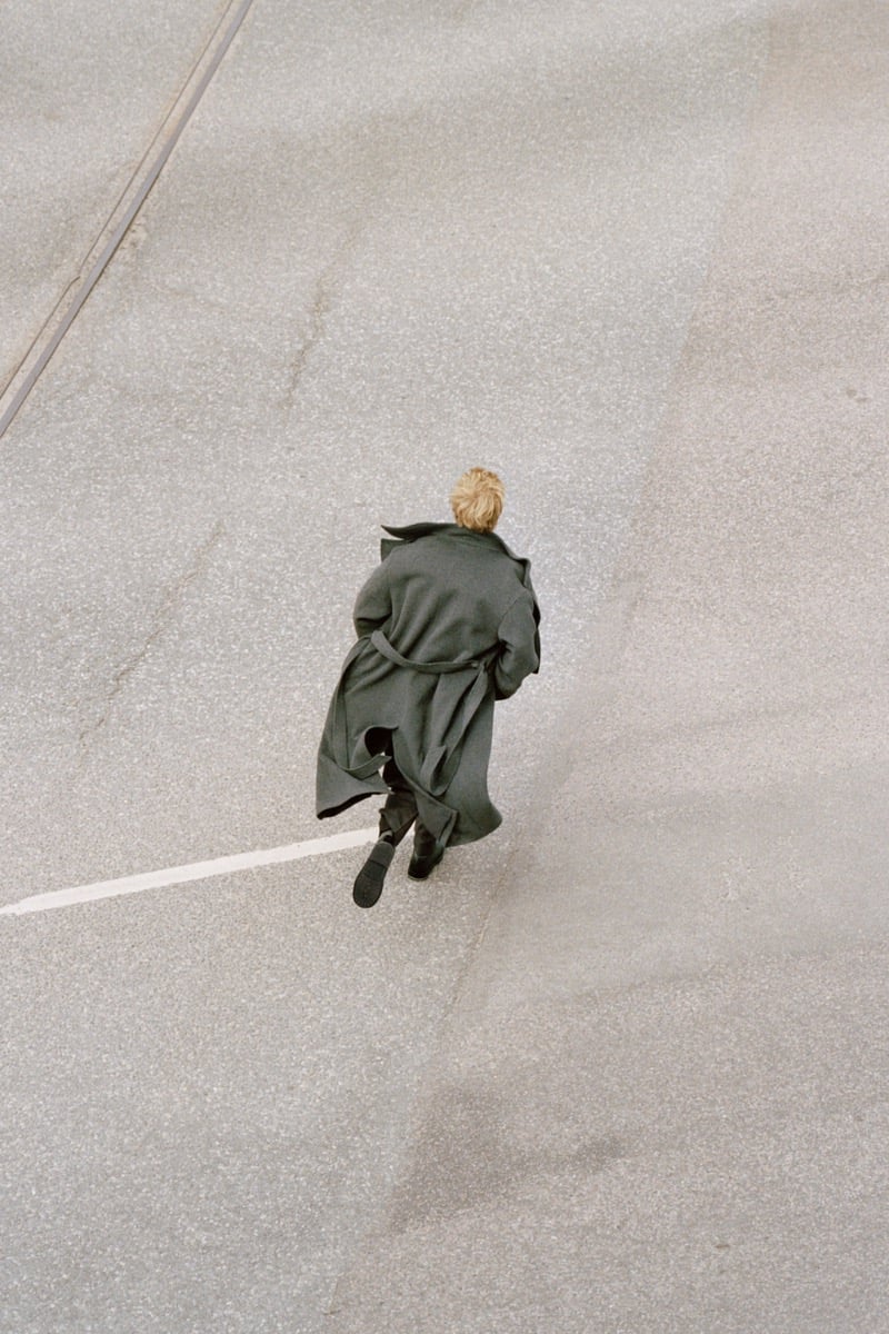 Overhead view of Pierrick Grégoire running across a street in a belted wool coat