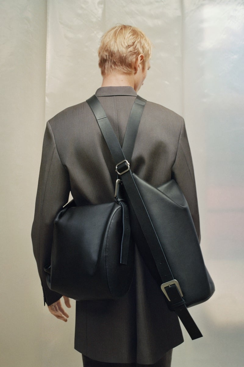 Pierrick Grégoire from behind in a suit jacket with a large leather bag strapped across his back